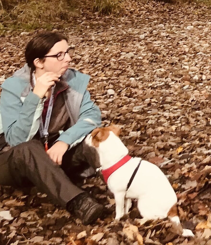 Picture of Heather sitting in autumn leaves with Penny, her jack russell next to her.