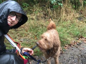 Wet dog walker holding a lead of a very soggy cockapoo